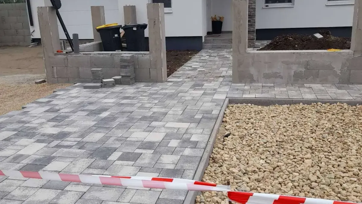 Frissen térkövezett bejáró és előkert egy új családi ház előtt, a kerítés lábazata mellett murvasávval